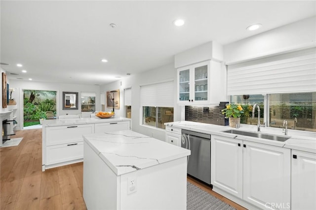 kitchen featuring a sink, a kitchen island, light wood-style floors, stainless steel dishwasher, and light stone countertops