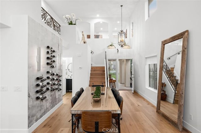 dining area with a chandelier, light wood-style flooring, a towering ceiling, baseboards, and stairway