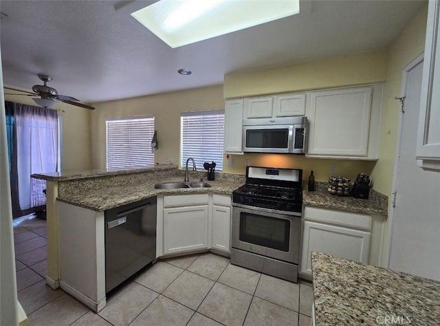 kitchen with light tile patterned floors, stainless steel appliances, white cabinets, a sink, and a peninsula