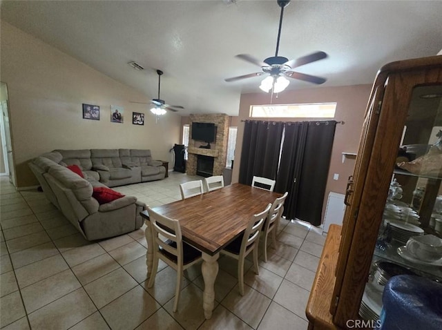 dining space with a stone fireplace, light tile patterned floors, ceiling fan, lofted ceiling, and visible vents