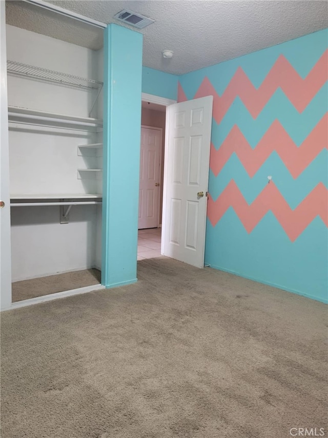 unfurnished bedroom featuring visible vents, carpet floors, a textured ceiling, and a closet