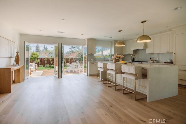 kitchen with a breakfast bar, an island with sink, light countertops, light wood-type flooring, and decorative backsplash