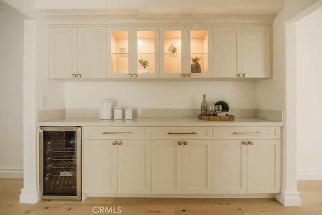 bar with wine cooler, light wood-style flooring, baseboards, and a dry bar