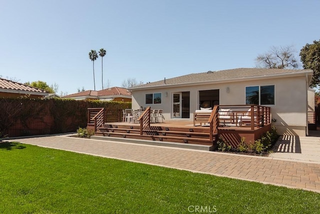 back of property with stucco siding, a lawn, a wooden deck, and fence