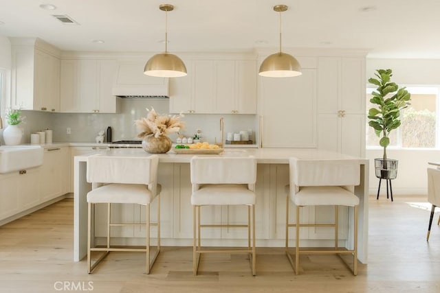 kitchen with visible vents, a kitchen island with sink, light countertops, light wood-style floors, and backsplash