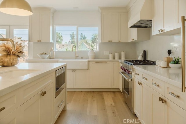 kitchen featuring custom range hood, light wood-style flooring, white cabinets, high end stainless steel range, and a sink