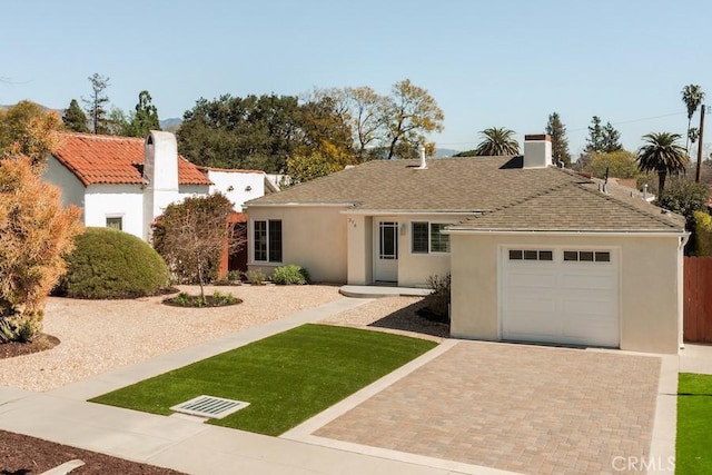 view of front of house with decorative driveway, a garage, a chimney, and stucco siding