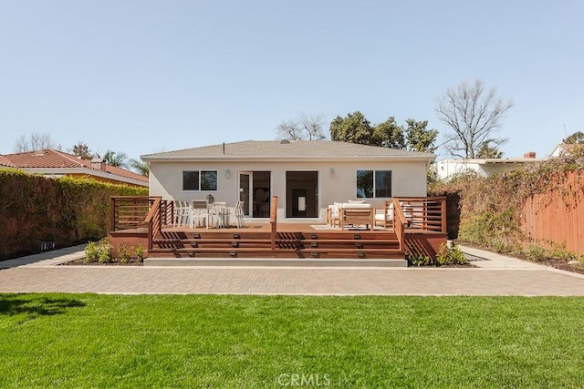 back of property with stucco siding, a lawn, fence, and a wooden deck