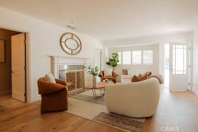 living area with visible vents, light wood-style flooring, a fireplace, and baseboards