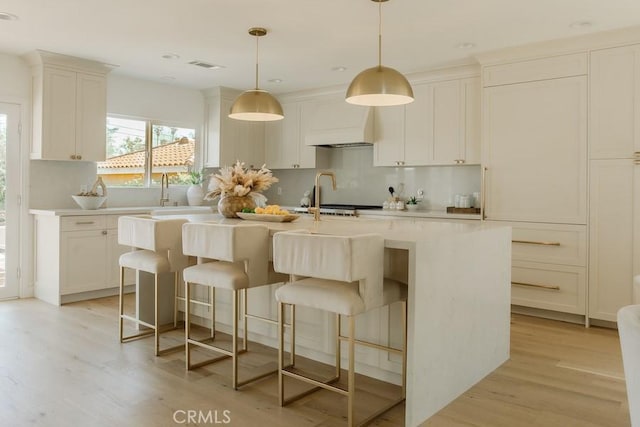 kitchen featuring light countertops, an island with sink, tasteful backsplash, and light wood finished floors