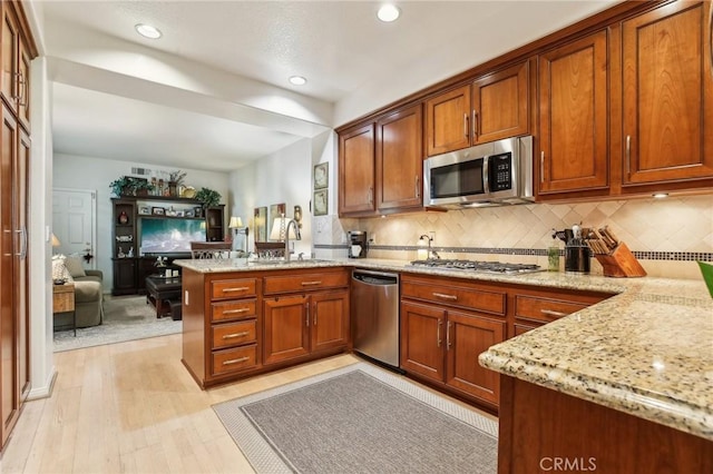 kitchen with stainless steel appliances, light stone counters, a peninsula, and a sink