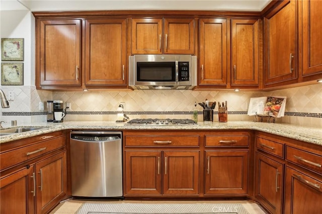 kitchen featuring appliances with stainless steel finishes, tasteful backsplash, a sink, and light stone countertops