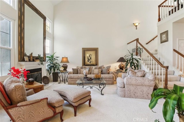 living room featuring stairway, a glass covered fireplace, a towering ceiling, and carpet