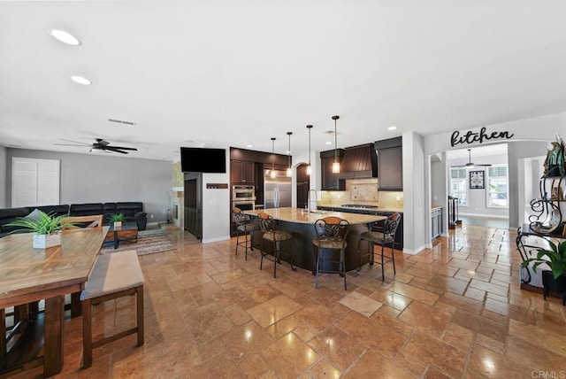 kitchen featuring ceiling fan, a kitchen bar, tasteful backsplash, recessed lighting, and premium range hood