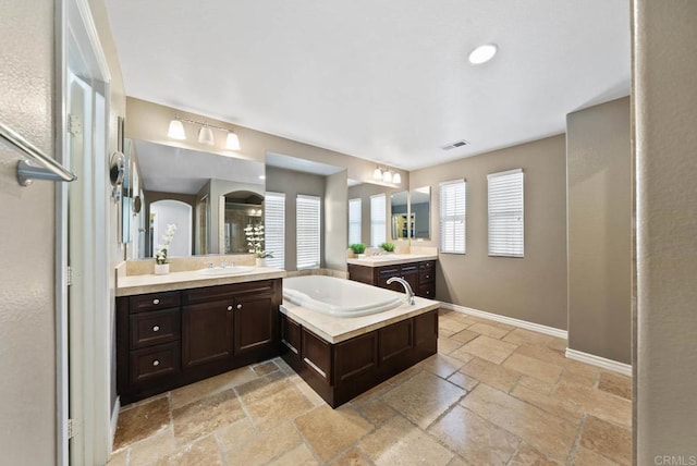 full bathroom featuring visible vents, a bath, baseboards, a sink, and stone tile floors