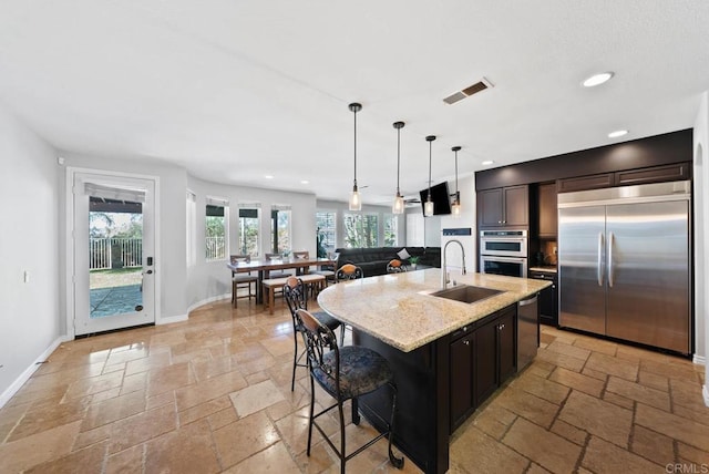 kitchen with appliances with stainless steel finishes, a sink, light stone countertops, and stone tile floors
