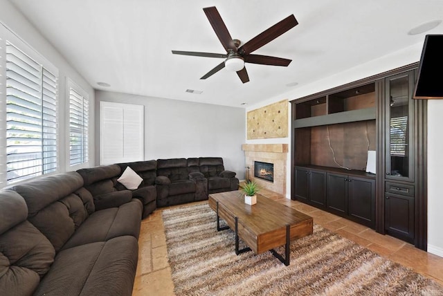 living room with a wealth of natural light, a tiled fireplace, visible vents, and ceiling fan