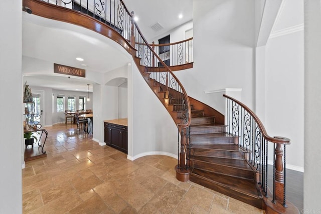 staircase featuring arched walkways, visible vents, a high ceiling, baseboards, and stone tile flooring