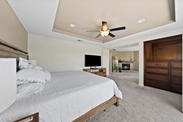 carpeted bedroom featuring baseboards, a lit fireplace, a ceiling fan, visible vents, and a raised ceiling