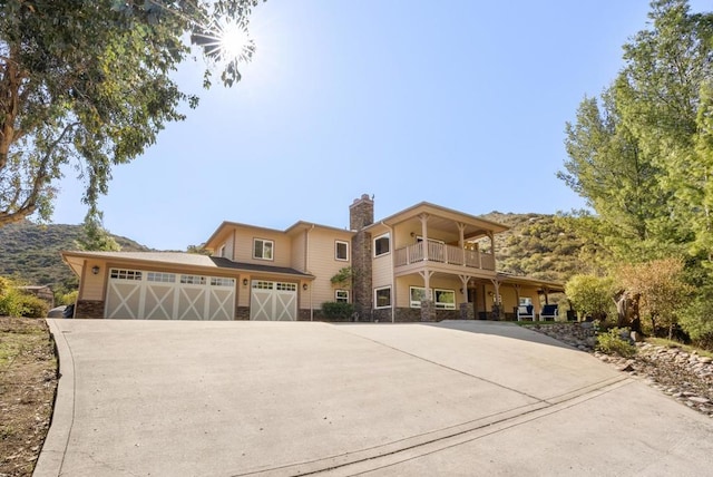 view of front of home featuring stone siding, a chimney, concrete driveway, and a balcony