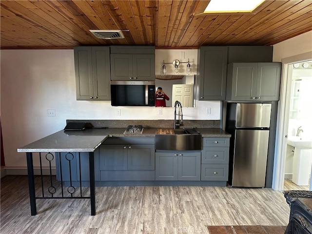 kitchen featuring dark countertops, gray cabinets, freestanding refrigerator, a sink, and wooden ceiling