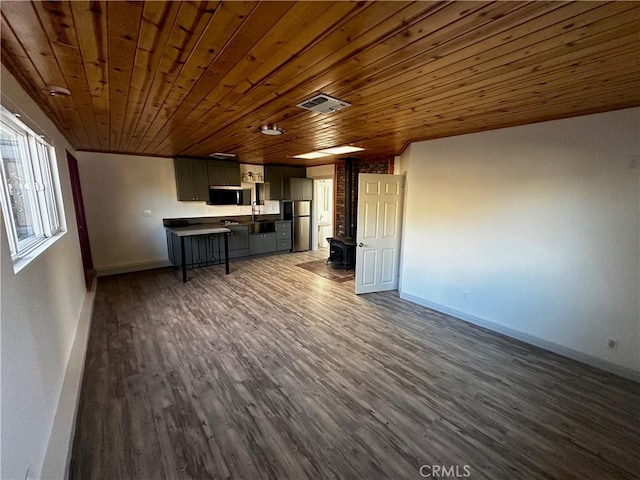 unfurnished living room with a wood stove, baseboards, visible vents, and dark wood-type flooring