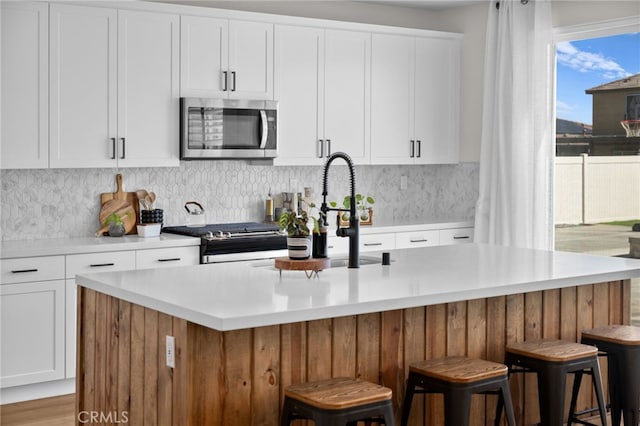 kitchen featuring white cabinets, stainless steel appliances, light countertops, and a kitchen breakfast bar