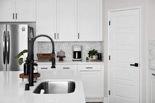 kitchen featuring a sink, white cabinets, light countertops, freestanding refrigerator, and decorative backsplash