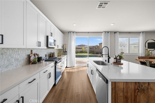 kitchen featuring a sink, visible vents, appliances with stainless steel finishes, decorative backsplash, and an island with sink