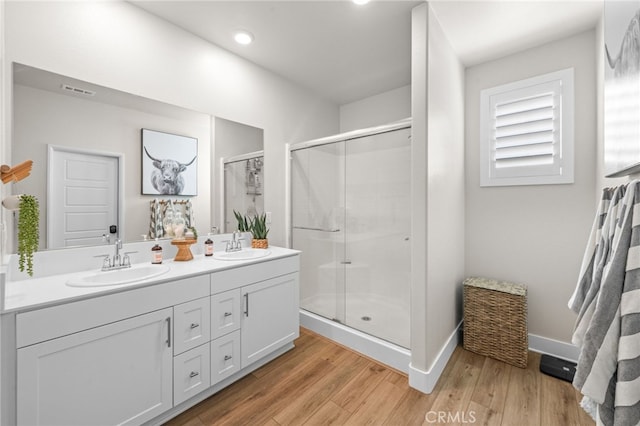 bathroom with double vanity, a shower stall, a sink, and wood finished floors