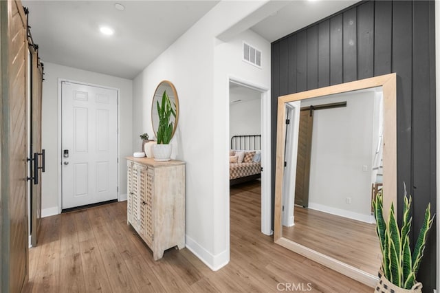 entrance foyer with a barn door, light wood-style flooring, visible vents, and baseboards