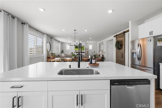 kitchen featuring a barn door, stainless steel appliances, a sink, white cabinetry, and open floor plan