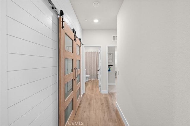 hallway with a barn door, light wood-style flooring, visible vents, and baseboards