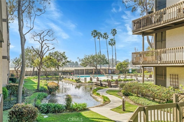 view of community featuring a swimming pool, a water view, and fence