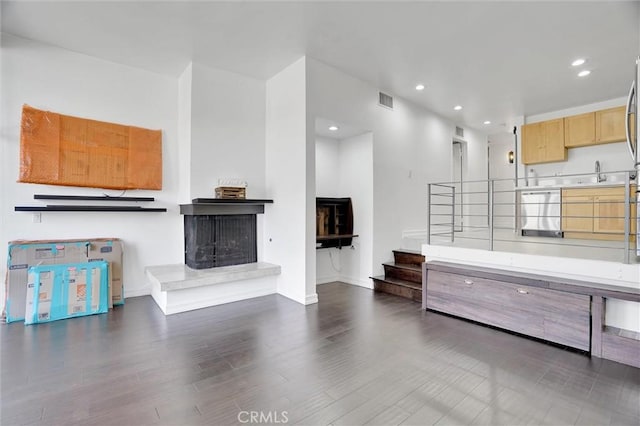 unfurnished living room with a fireplace with raised hearth, wood finished floors, stairs, a sink, and recessed lighting