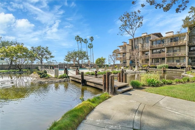 view of dock featuring a water view, fence, and a community pool