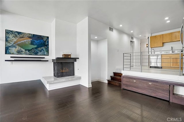 living room with visible vents, a fireplace with raised hearth, dark wood-style flooring, recessed lighting, and stairs