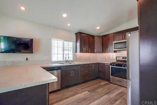 kitchen featuring dark brown cabinetry, stainless steel appliances, a sink, vaulted ceiling, and decorative backsplash