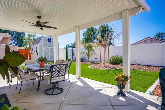 view of patio / terrace featuring ceiling fan, outdoor dining area, a fenced backyard, a storage shed, and an outdoor structure