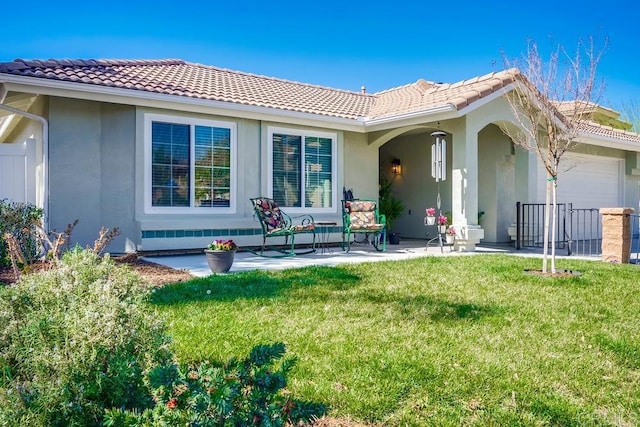 rear view of property featuring a lawn, an attached garage, a tile roof, and stucco siding