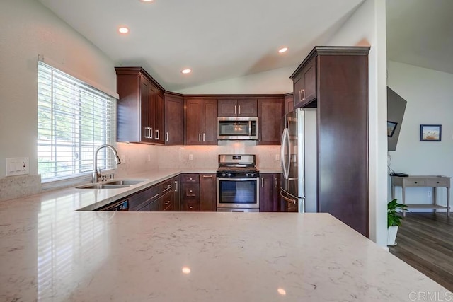 kitchen featuring stainless steel appliances, lofted ceiling, backsplash, a sink, and light stone countertops