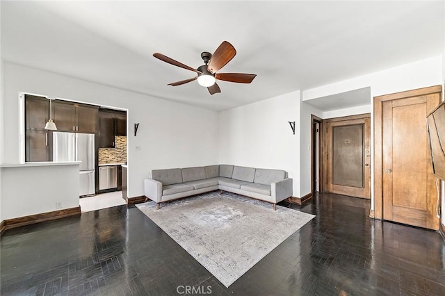 unfurnished living room with a ceiling fan and baseboards