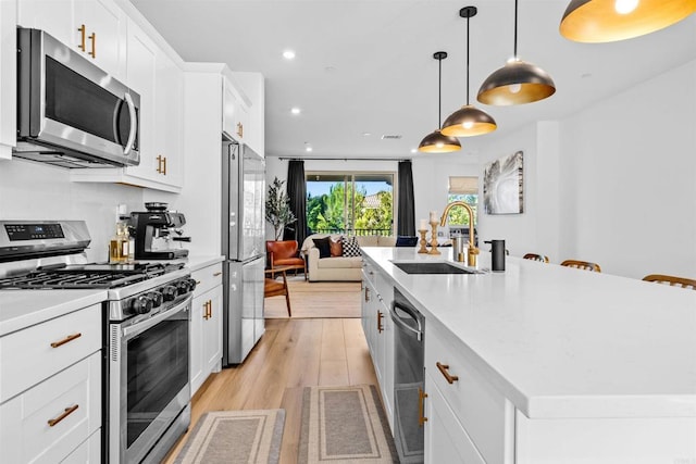 kitchen with stainless steel appliances, a sink, white cabinets, light countertops, and a center island with sink