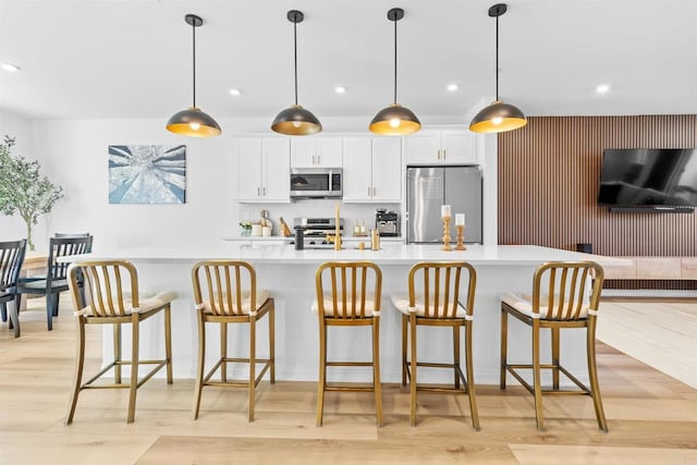 kitchen with light wood-style flooring, white cabinets, light countertops, appliances with stainless steel finishes, and a large island with sink