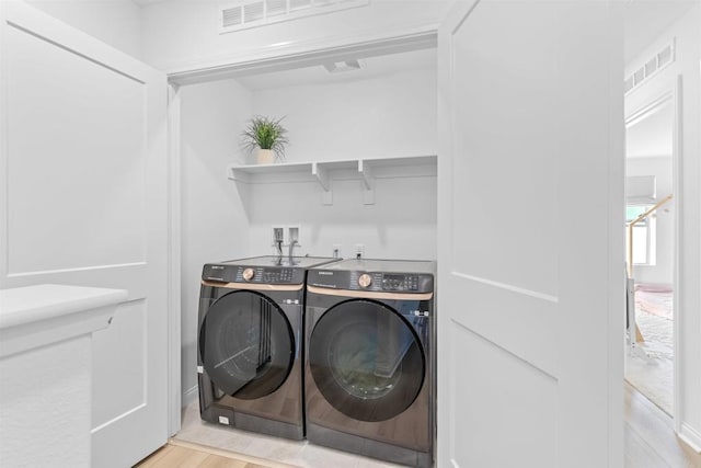 clothes washing area with laundry area, light wood-type flooring, visible vents, and washer and dryer