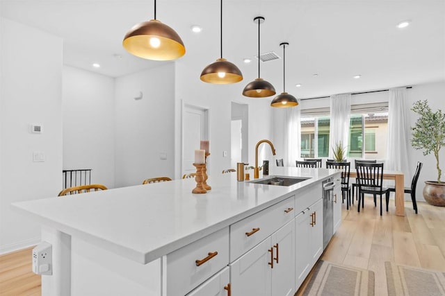 kitchen with a kitchen island with sink, light wood-type flooring, a sink, and visible vents