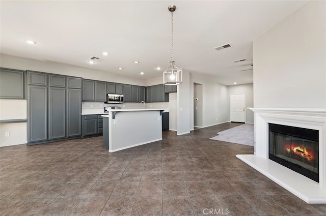 kitchen with visible vents, a glass covered fireplace, stainless steel microwave, light countertops, and gray cabinetry