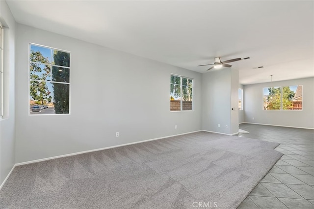 carpeted empty room with ceiling fan, tile patterned floors, visible vents, and baseboards