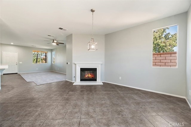 unfurnished living room with baseboards, visible vents, a ceiling fan, and a glass covered fireplace