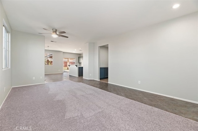 unfurnished living room featuring a ceiling fan, dark carpet, dark tile patterned floors, and baseboards